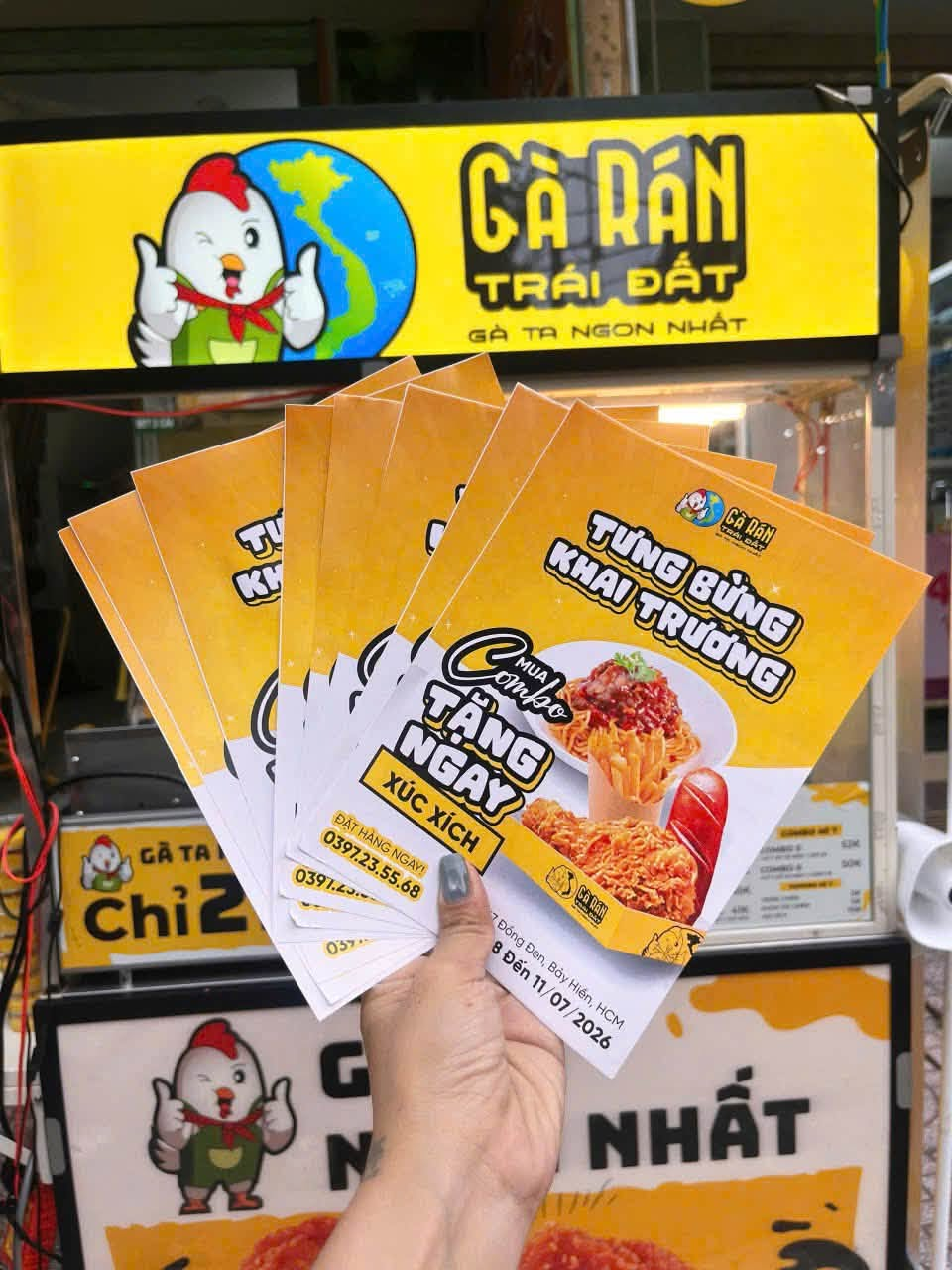 Gà Rán Trái Đất store sign with the chicken mascot and opening-day flyers